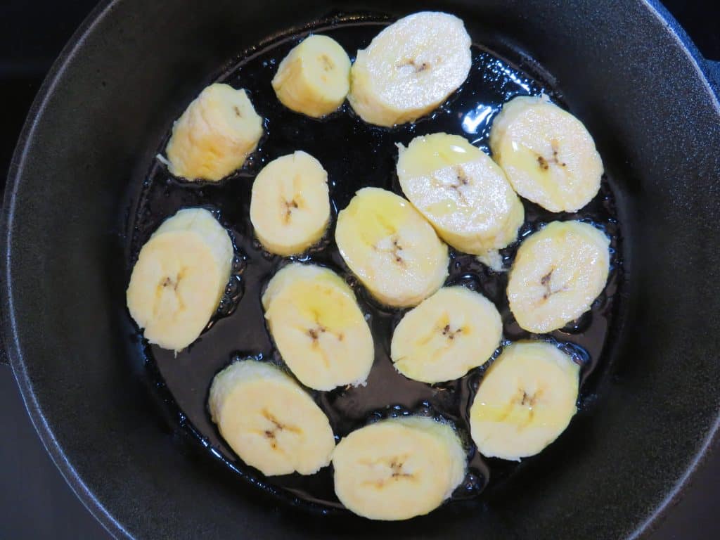 Uncooked plantains in a cast iron skillet.