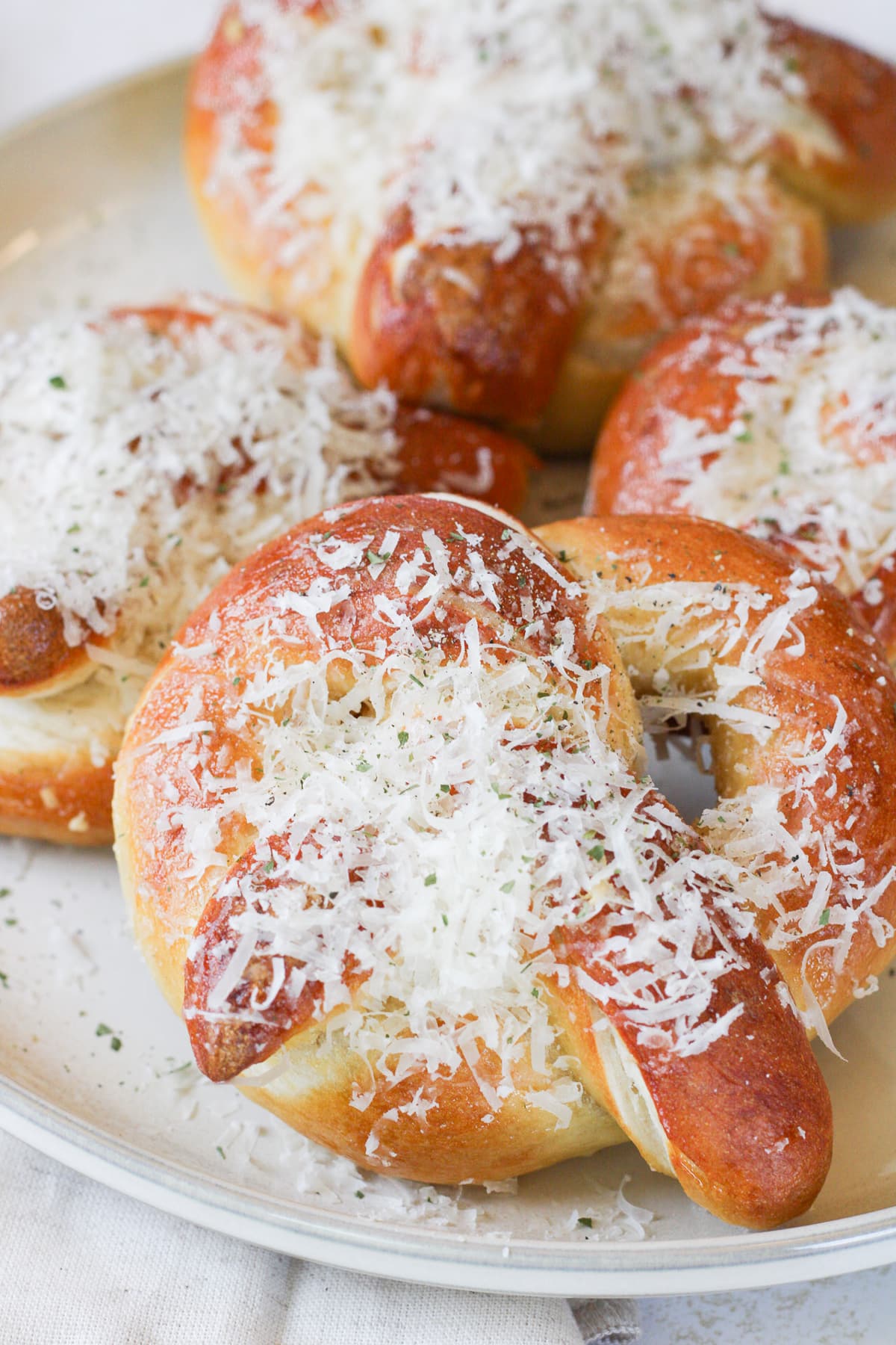 Close up image of a homemade garlic parmesan soft pretzel on a plate topped with parmesan cheese.