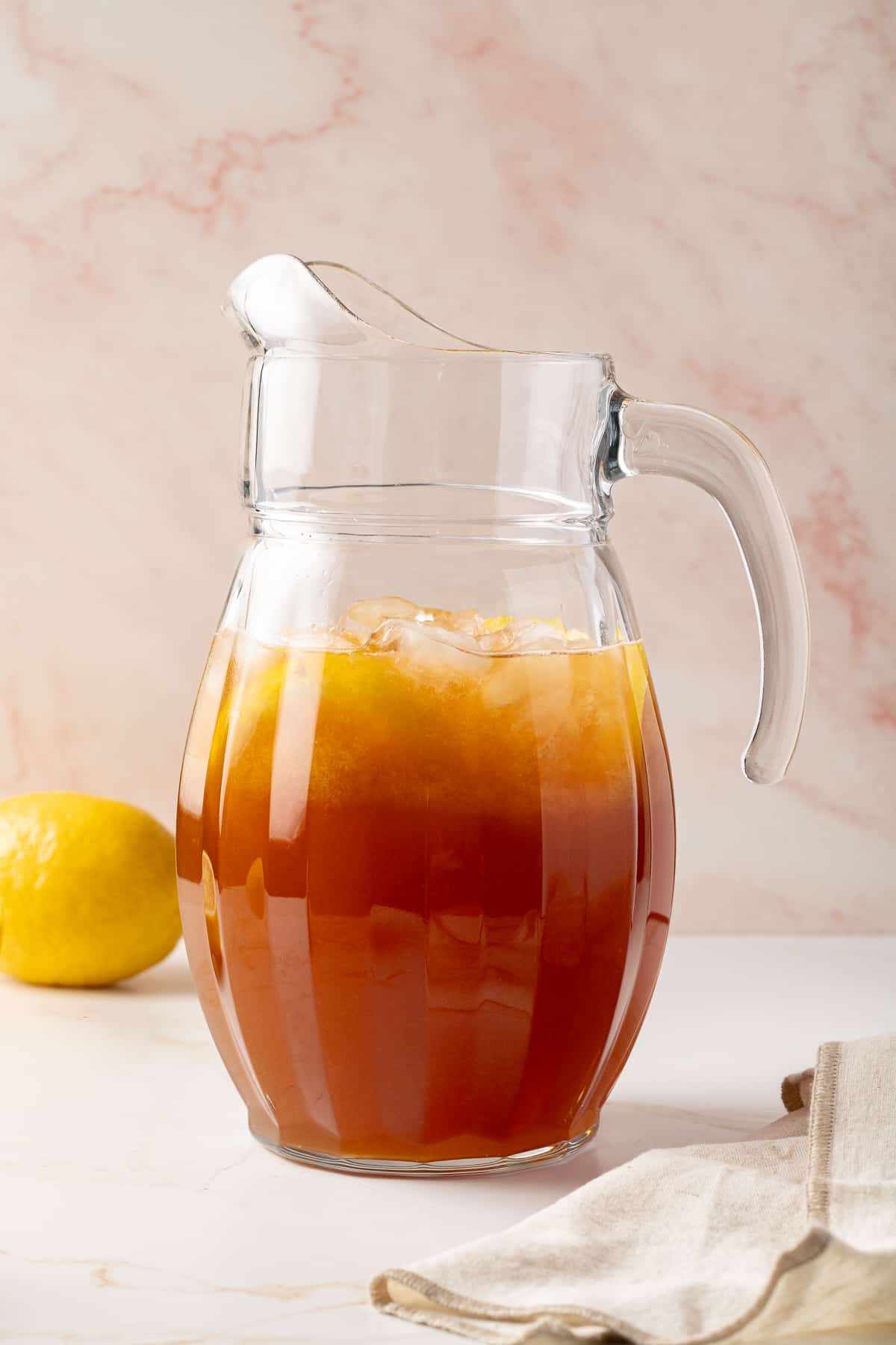 Iced tea in a pitcher with a lemon in the background.