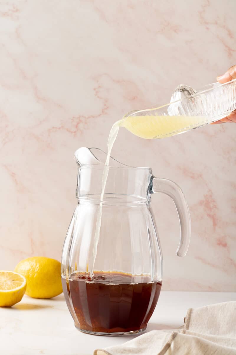 Hand pouring lemon juice in a pitcher with iced tea.