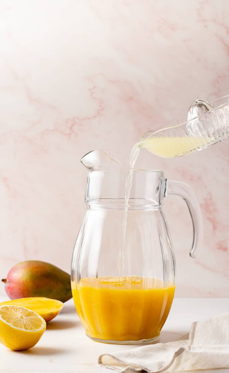 Mango puree in a pitcher with lemon juice being poured in.