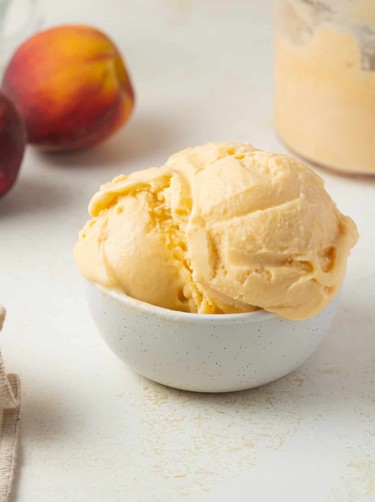 Close up of peach ice cream in a bowl with fresh peaches in the background.
