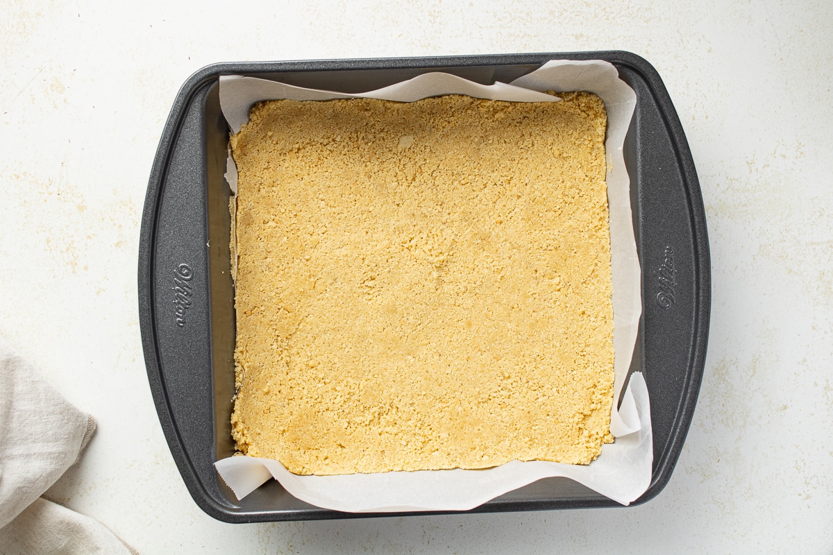 Graham cracker crust in a cake pan with parchment paper.